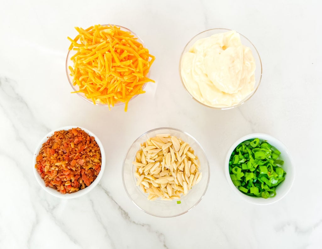 all the ingredients for Neiman Marus dip laid out on a table, including shredded cheese, mayo, bacon, slivered almonds and green oniond