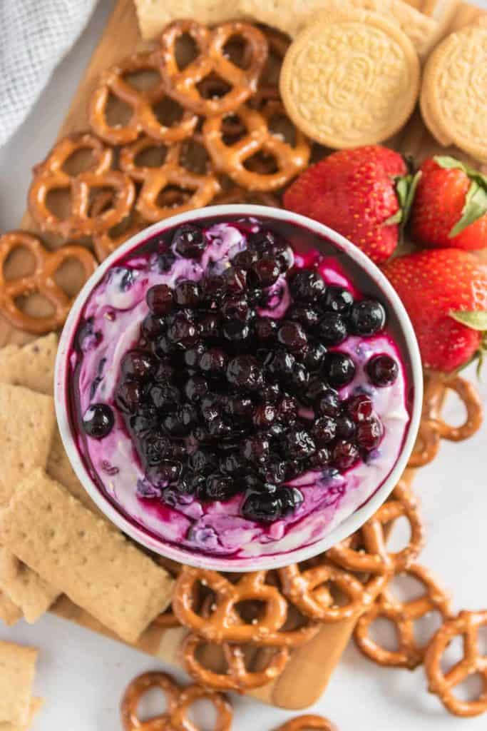 overhead shot of blueberry cheesecake dip with strawberries and pretzels