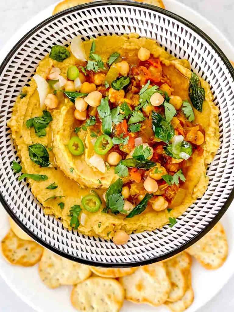 chole masala hummus dip in a bowl with garnish surrounded by crackers for dipping