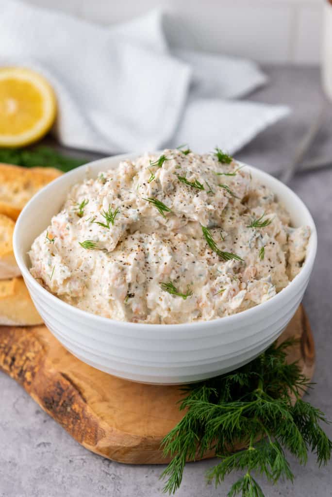 salmon cream cheese dip in a white bowl sitting on a cutting board