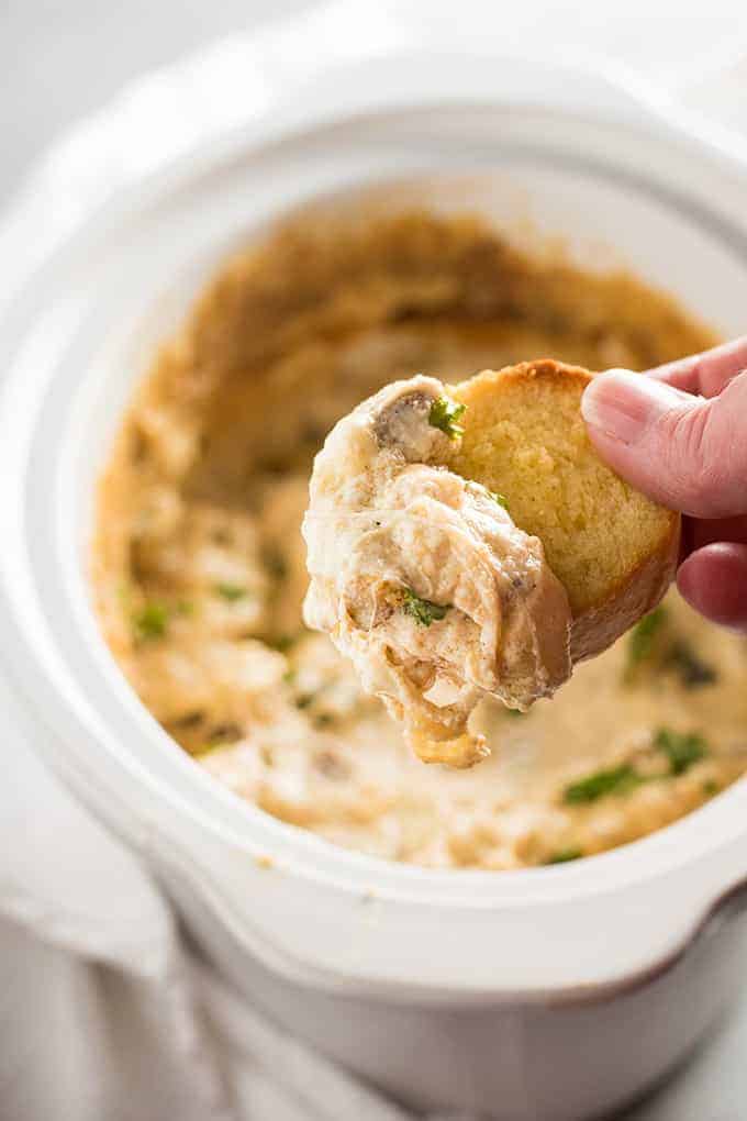 baguette slice being dipped into philly cheesesteak dip made in a crock pot