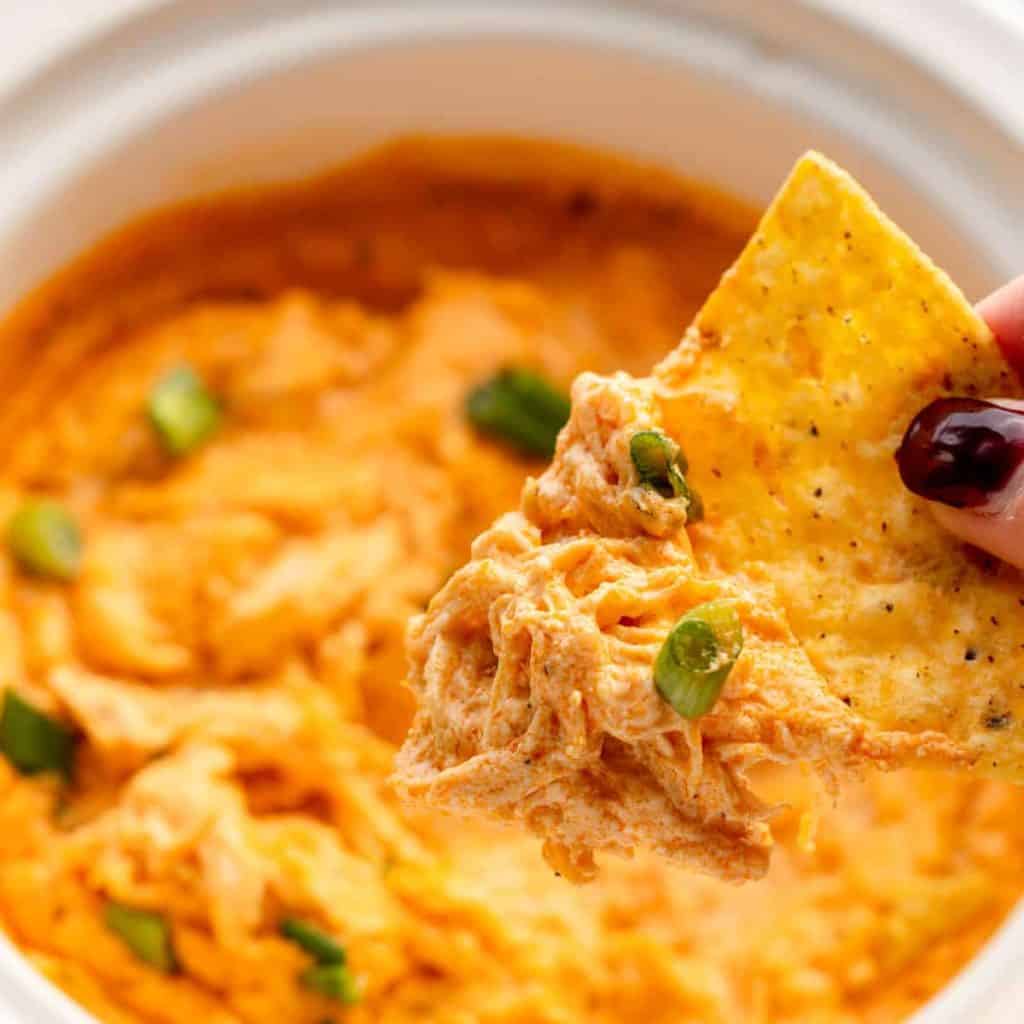 tortilla chip being dipped in buffalo chicken dip made in the crockpot