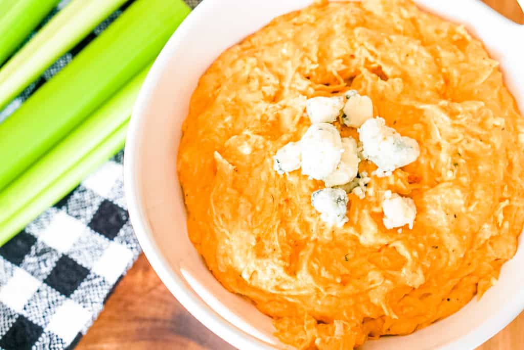 buffalo chicken dip in a bowl with blue cheese crumbles and celery on the side