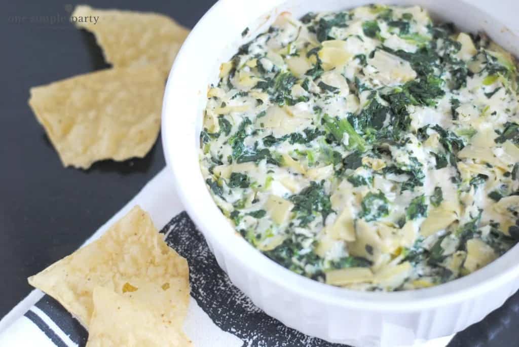 spinach artichoke dip in a white bowl with white corn chips on the side
