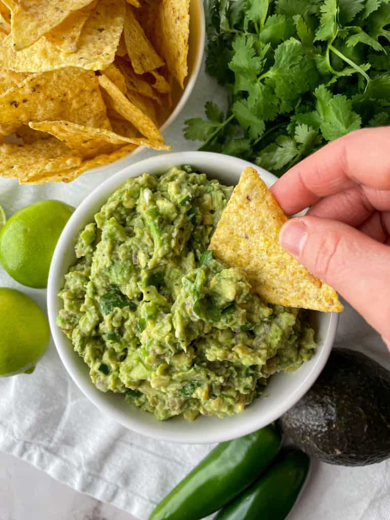 tortilla chip being dipped in guac without tomatoes