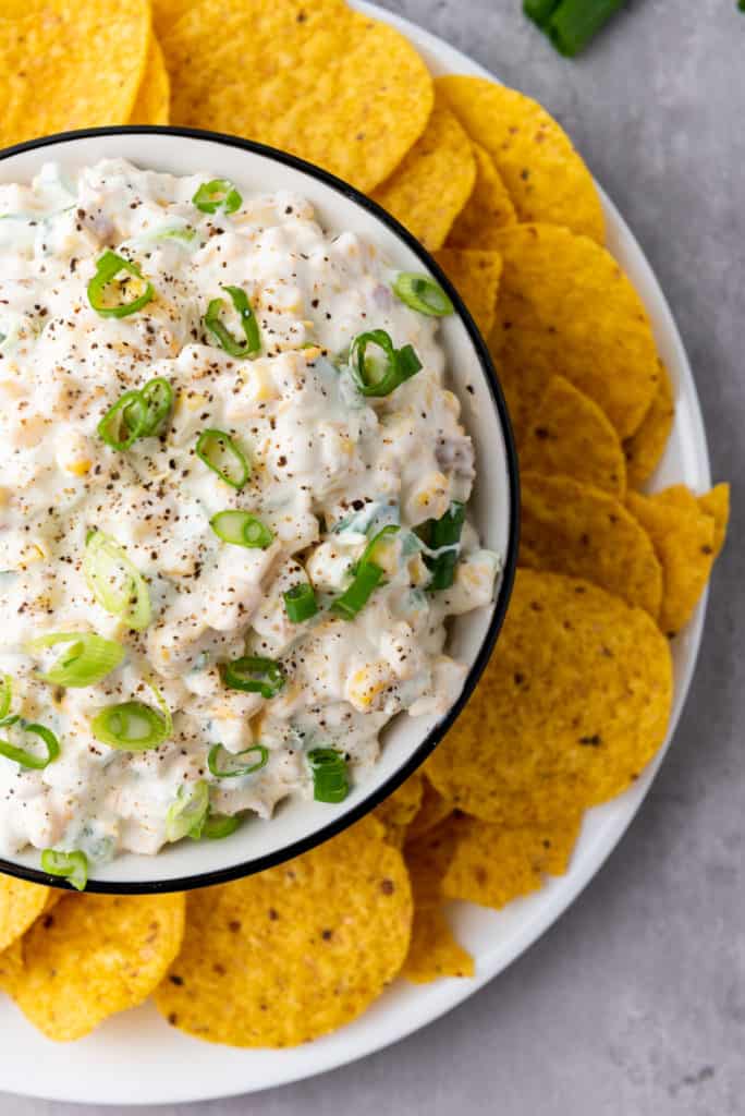 up close photo of chilled corn dip recipe in a bowl surrounded by tortilla chips