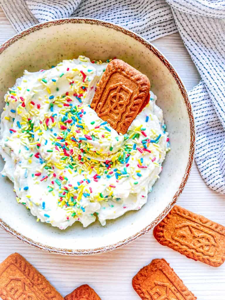 funfetti dip with colorful candy sprinke in a bowl with an almond cookie