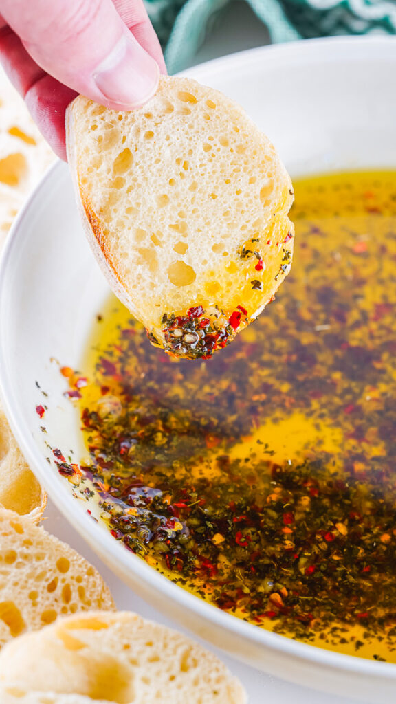 french baguette slice being dipped in homemade bread dipping oil