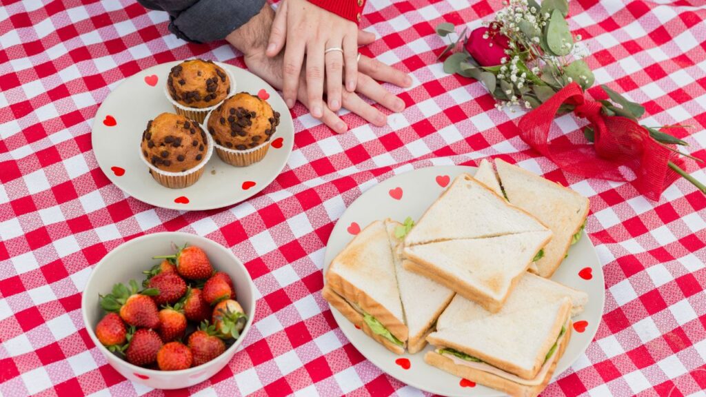 Couple holding hands on checkered coverlet with food