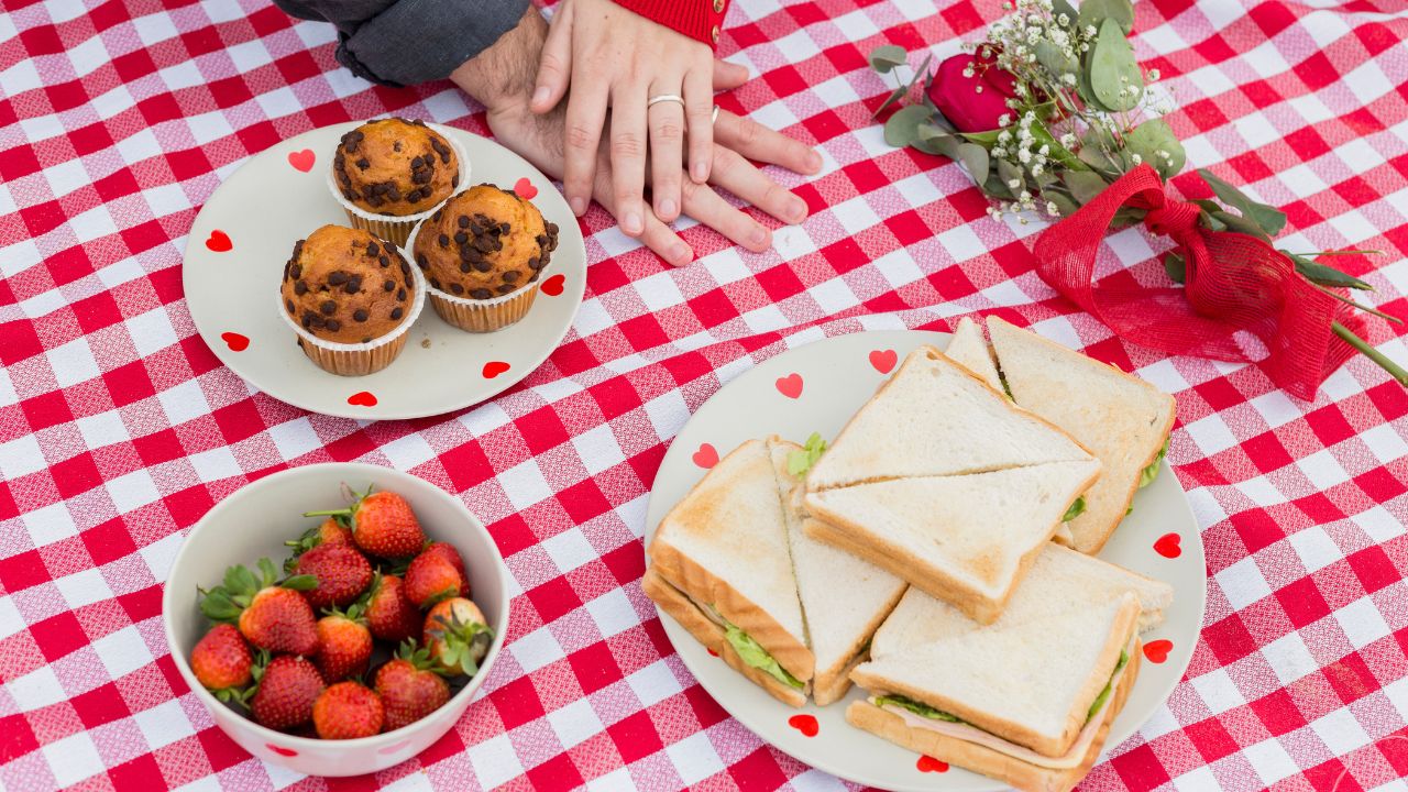 Couple holding hands on checkered coverlet with food