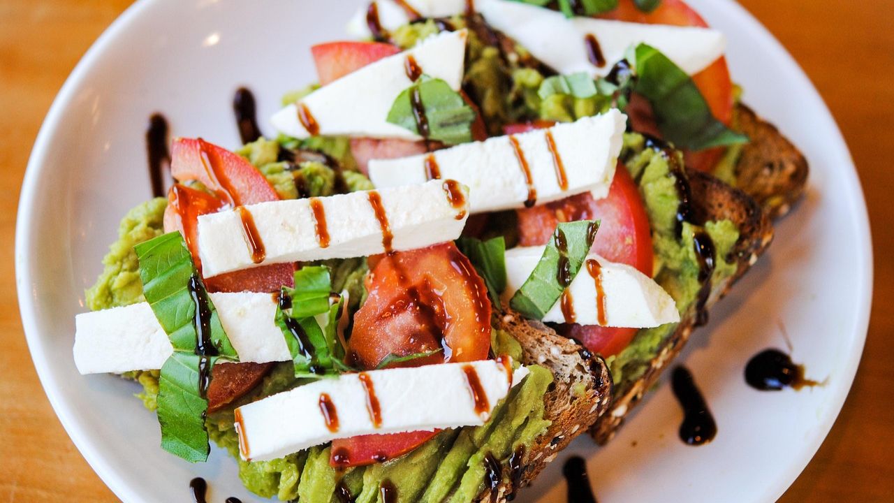 Avocado toast topped with tomato, basil, mozzarella, and balsamic glaze
