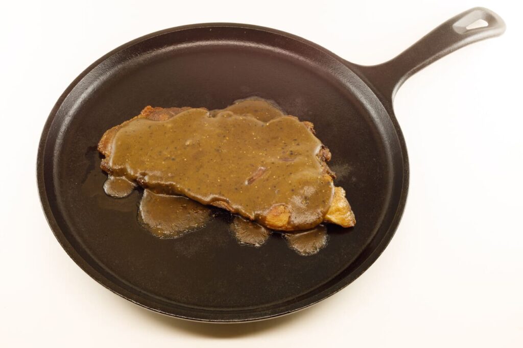 Ham steak with red-eye gravy served on a cast iron skillet. Isolated on a white background