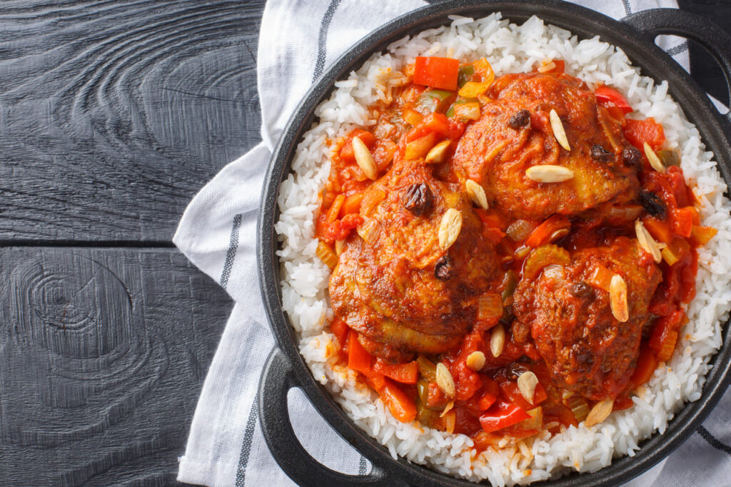 Southern American Country Captain chicken fried and stewed with vegetables, tomato sauce and curry, served with rice in a frying pan on the table. Horizontal top view from above