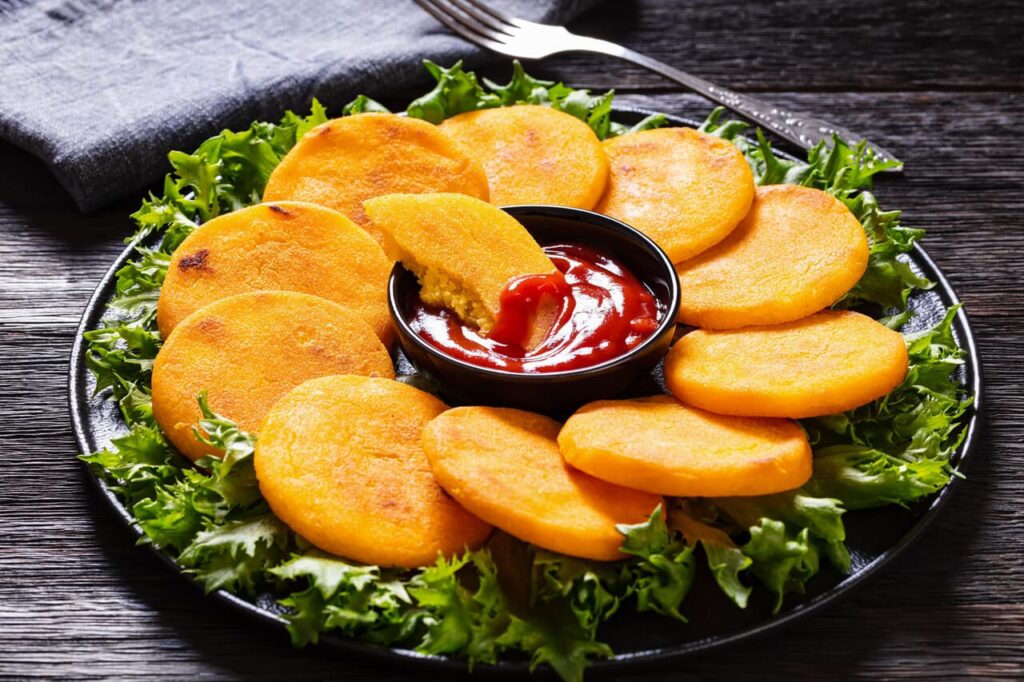 Hot Water Cornbread, corn pones, hoecakes, corn dodgers on black plate with ketchup and lettuce on dark wood table