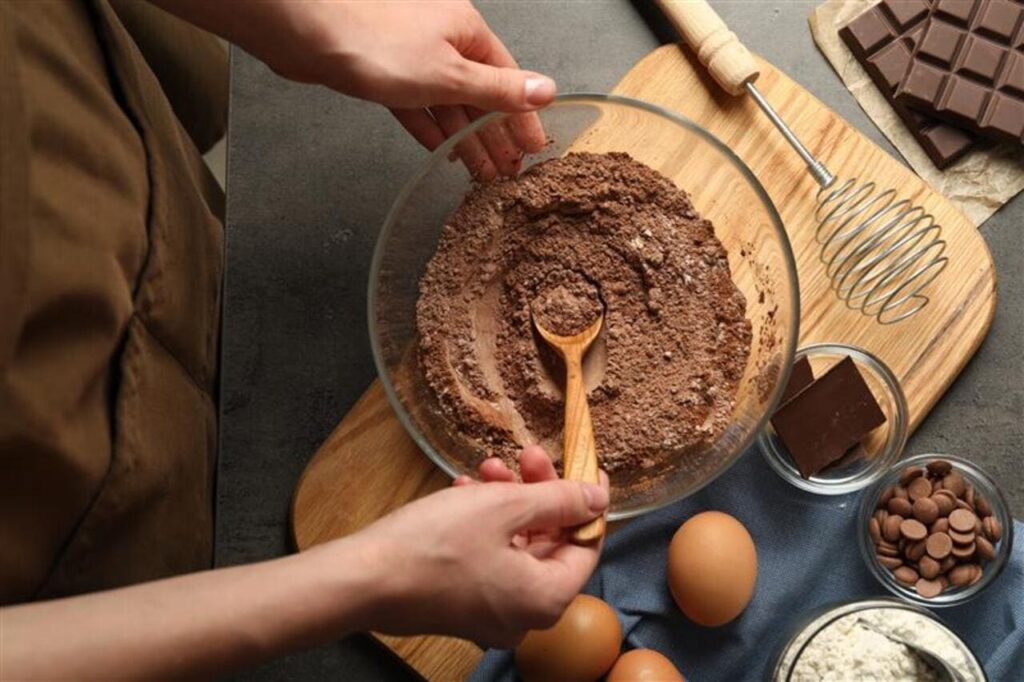 A spatula folding large dark chocolate chunks into brownie batter.
