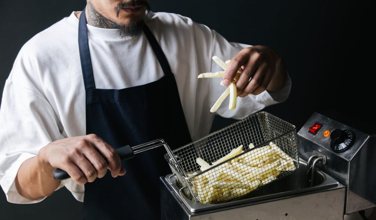A Man in White Shirt with Black Apron Holding a Strainer with French Fries