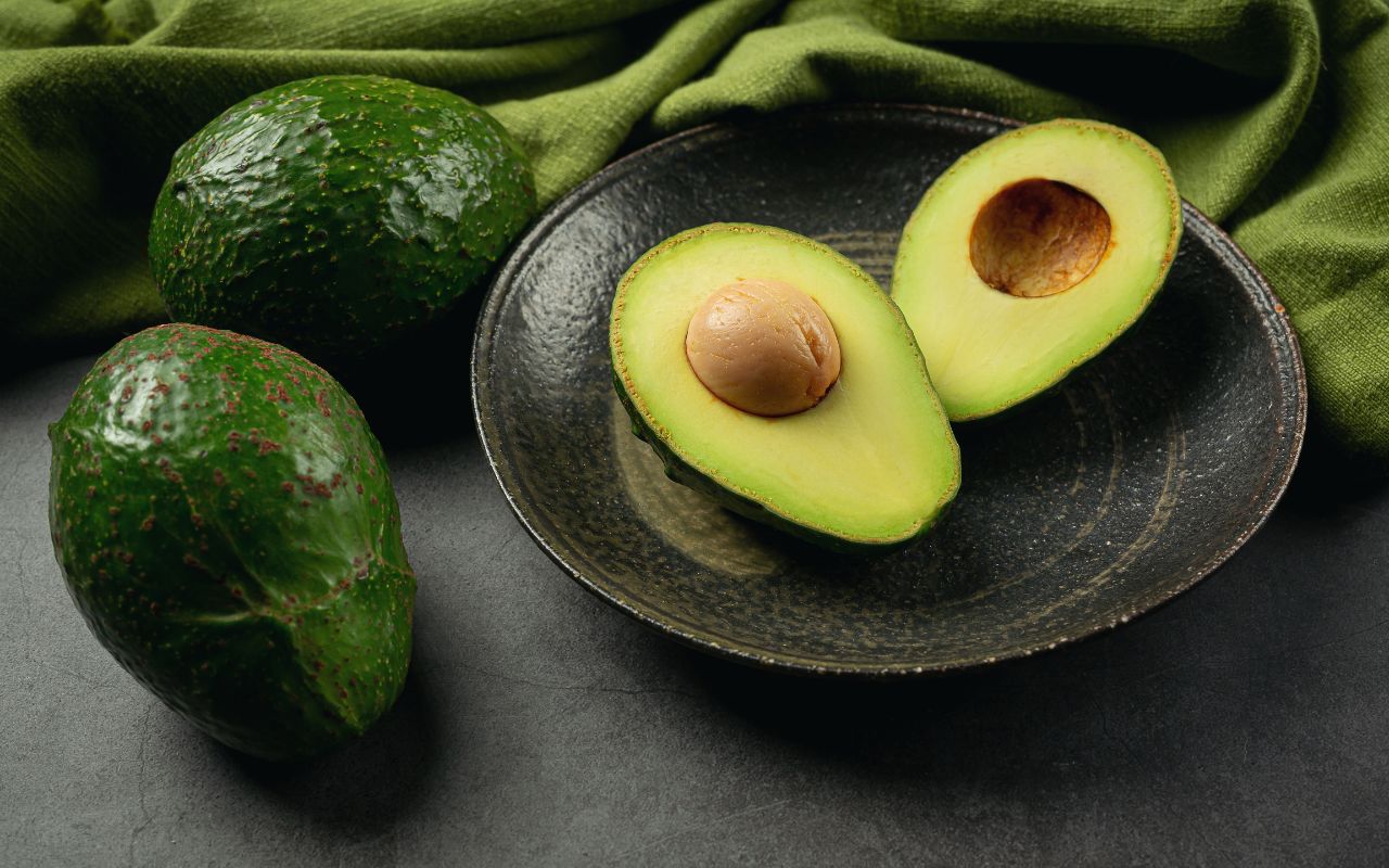 Halved avocado on a dark plate with whole avocados nearby