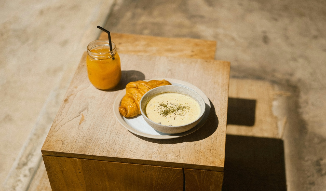Bowl of Soup with Croissant and a Jar of Juice Standing on a Table