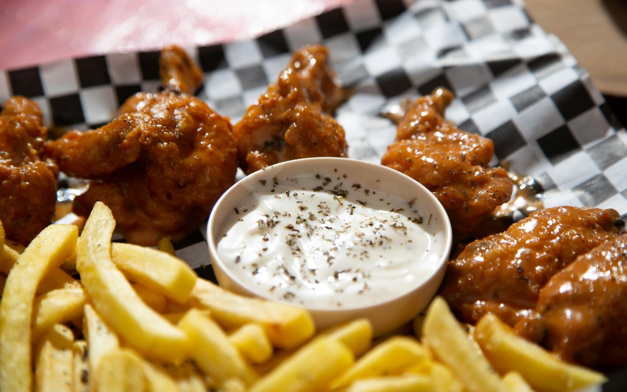 Buffalo chicken wings with fries and a cup of ranch/blue cheese dip on a checkered tray