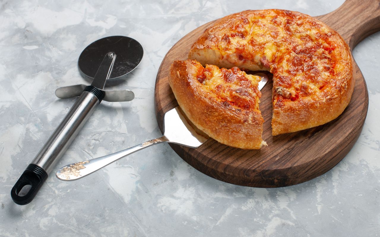 Deep-dish pizza with a slice served on a wooden board