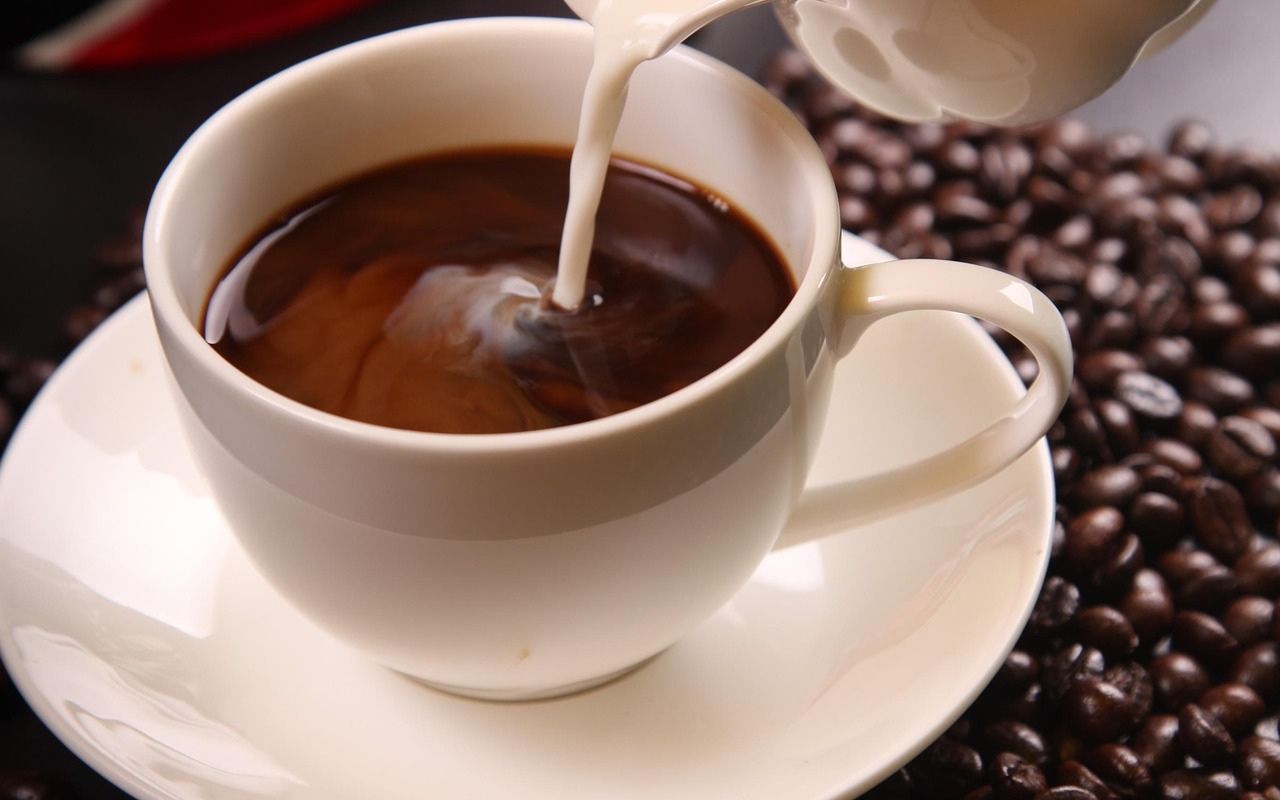 Cream pouring into a white cup of coffee