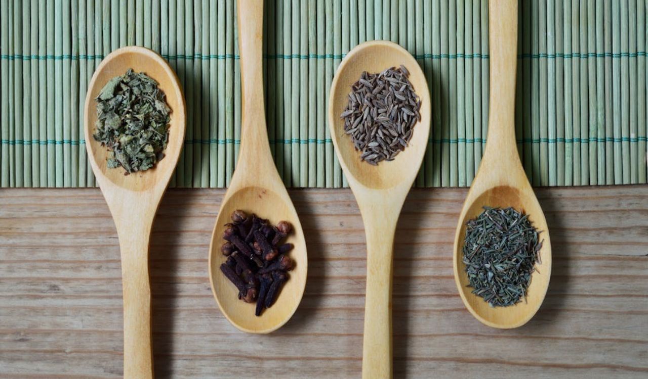 Brown Wooden Spoon With Herbs on Top of Green Bamboo Mat and Brown Wooden Surface