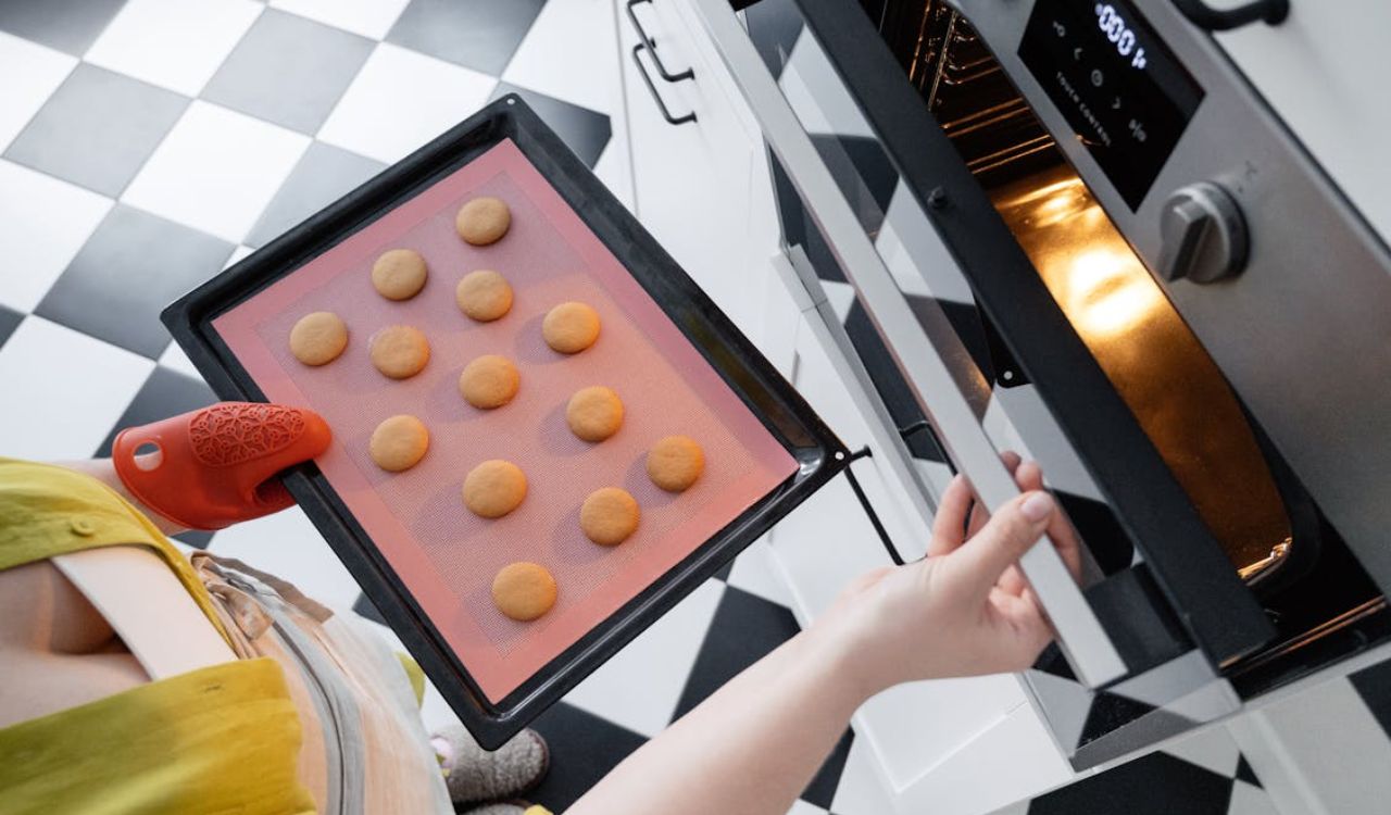 Crop woman putting cookies in oven in kitchen