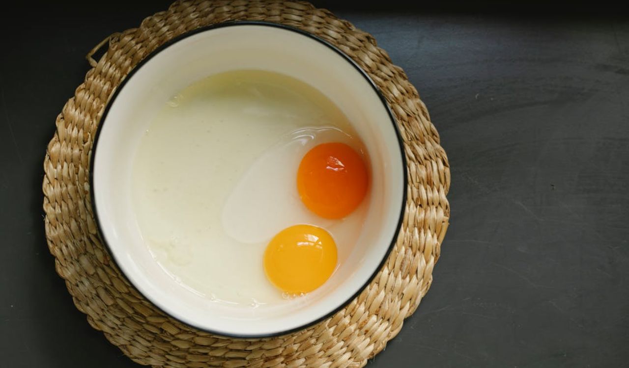 Uncooked broken eggs in bowl placed on wicker table mat