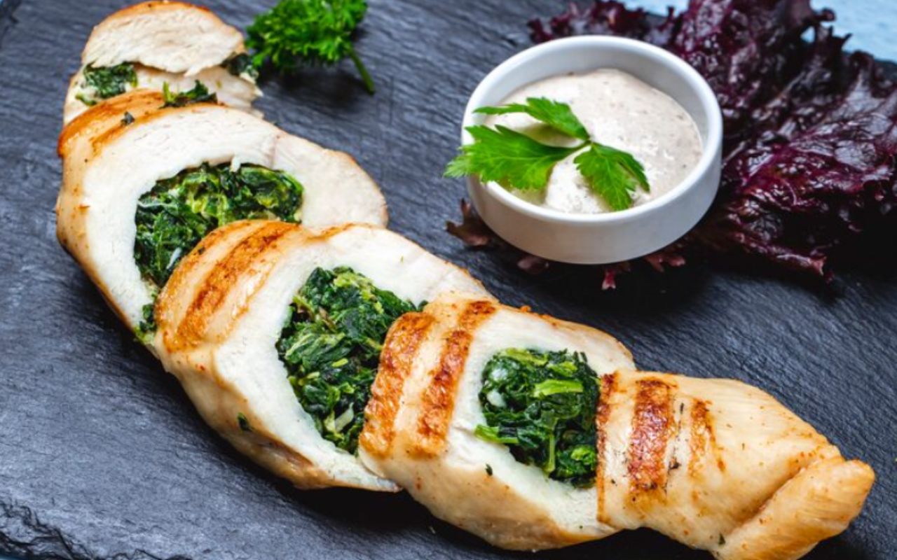 Side view chicken breast stuffed with spinach and sauce on the table