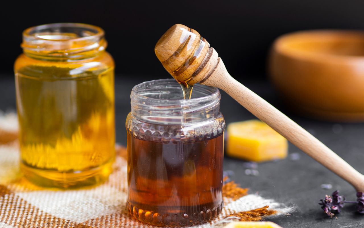 Honey dipper drizzling into a glass jar of honey