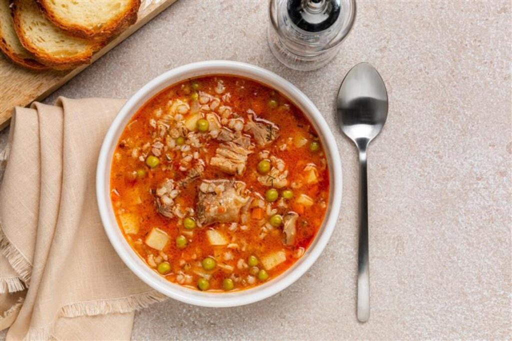 Beef barley soup with vegetables, potato, green peas, carrot, celery, onion and tomato. Bread. Directly above.