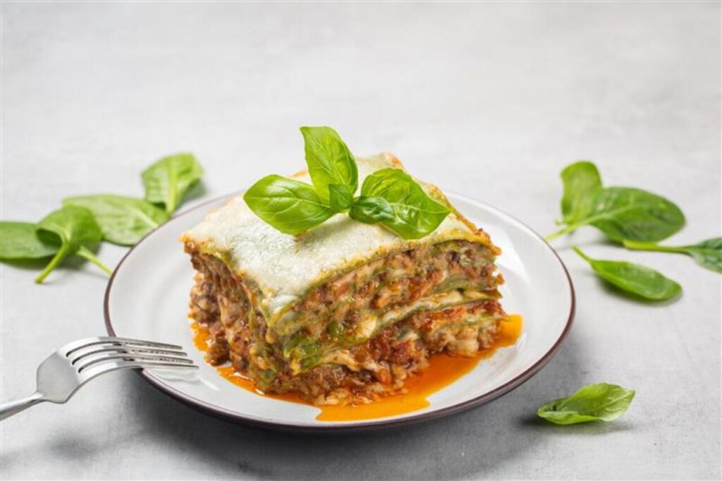 A slice of lasagna with visible layers of pasta, ragù, béchamel, and Parmigiano.