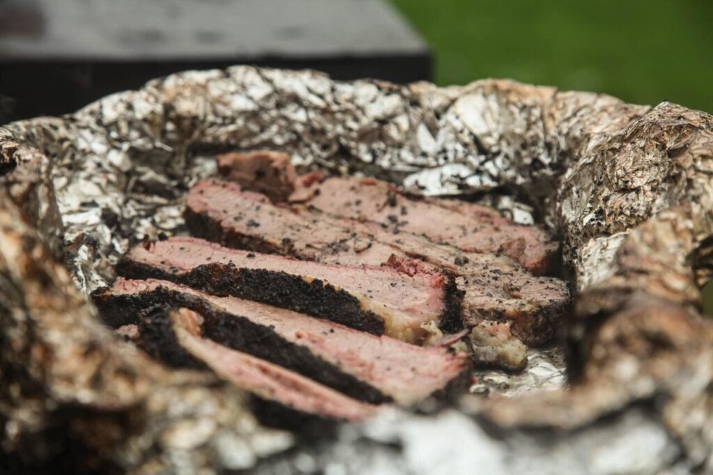 A brisket wrapped tightly in butcher paper on a smoker rack.