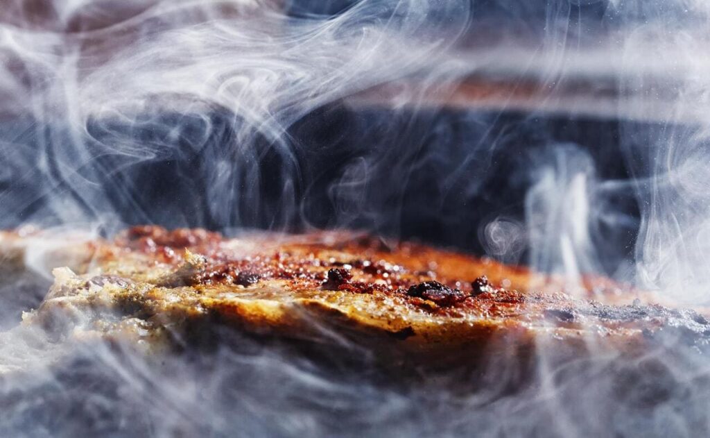 Brisket smoking inside a smoker with visible wood smoke swirling around.