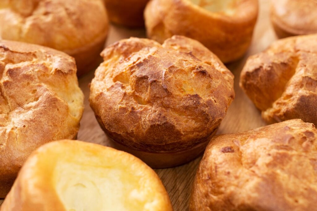 A lot of fresh hot popovers on wood plate or wooden board. Easy cooking, tasty breakfast, close up.