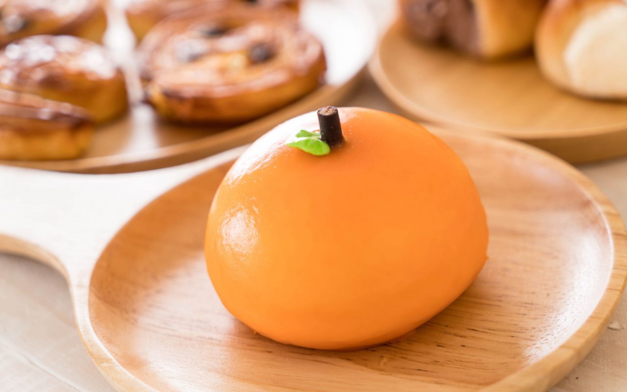 Orange-colored pumpkin-shaped dessert with a green leaf and a brown stem on a wooden plate