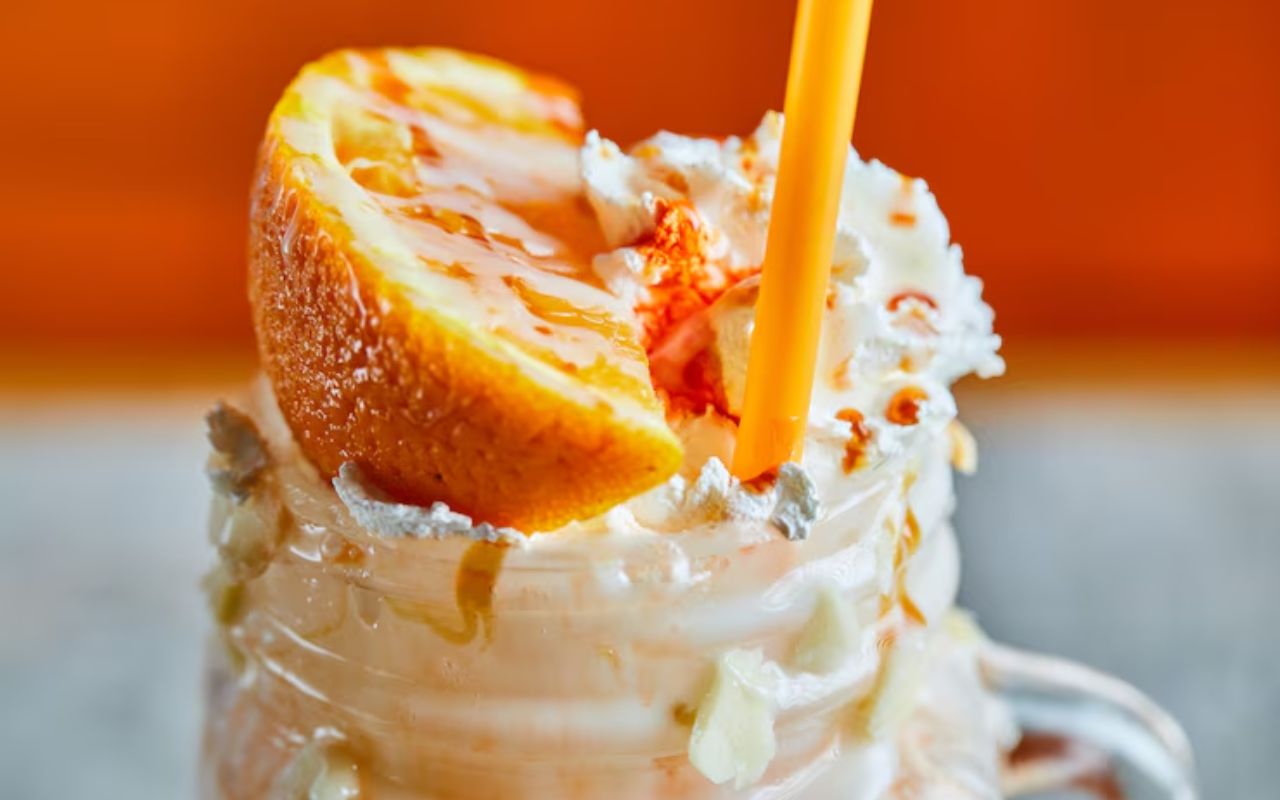 Orange mousse topped with whipped cream and an orange slice, with a straw