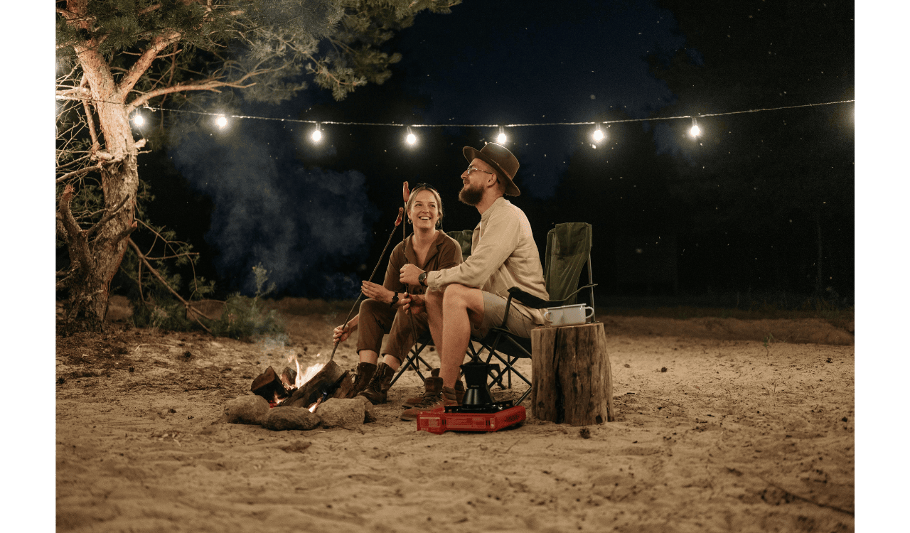A Couple Sitting on Chair while Grilling on Campfire
