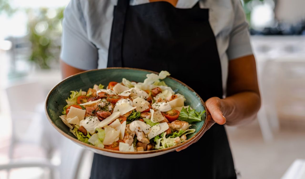Person holding ceramic plate with Caesar salad
