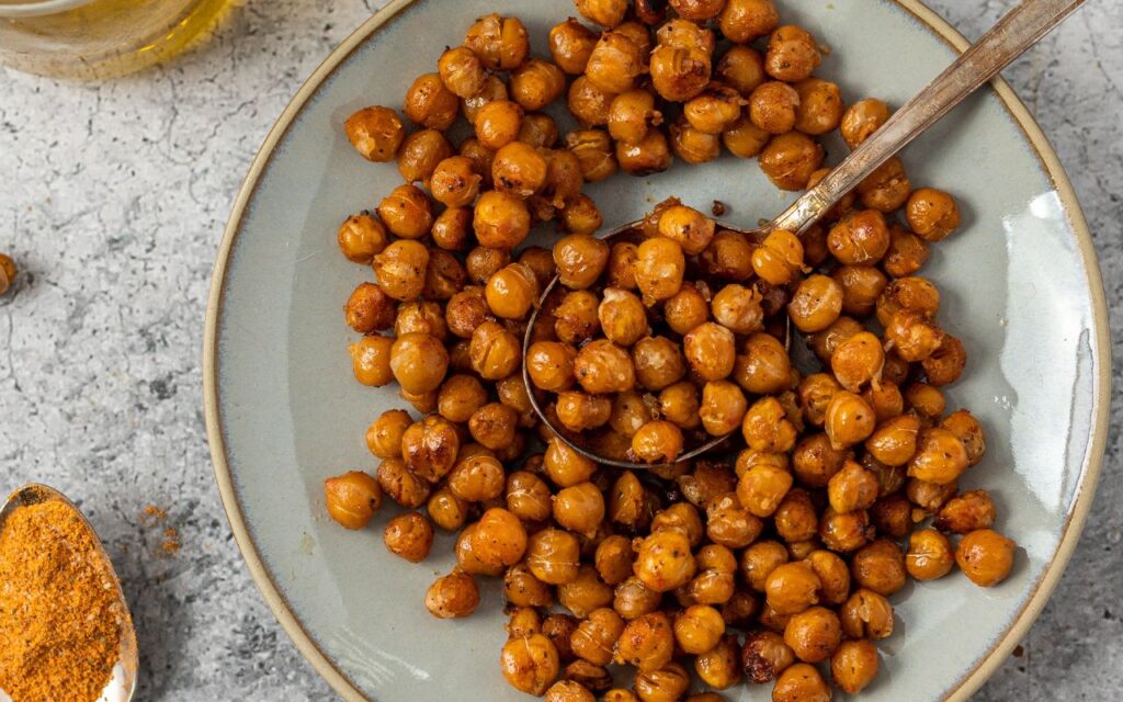 Bowl of seasoned roasted chickpeas with a spoon, served on a grey plate