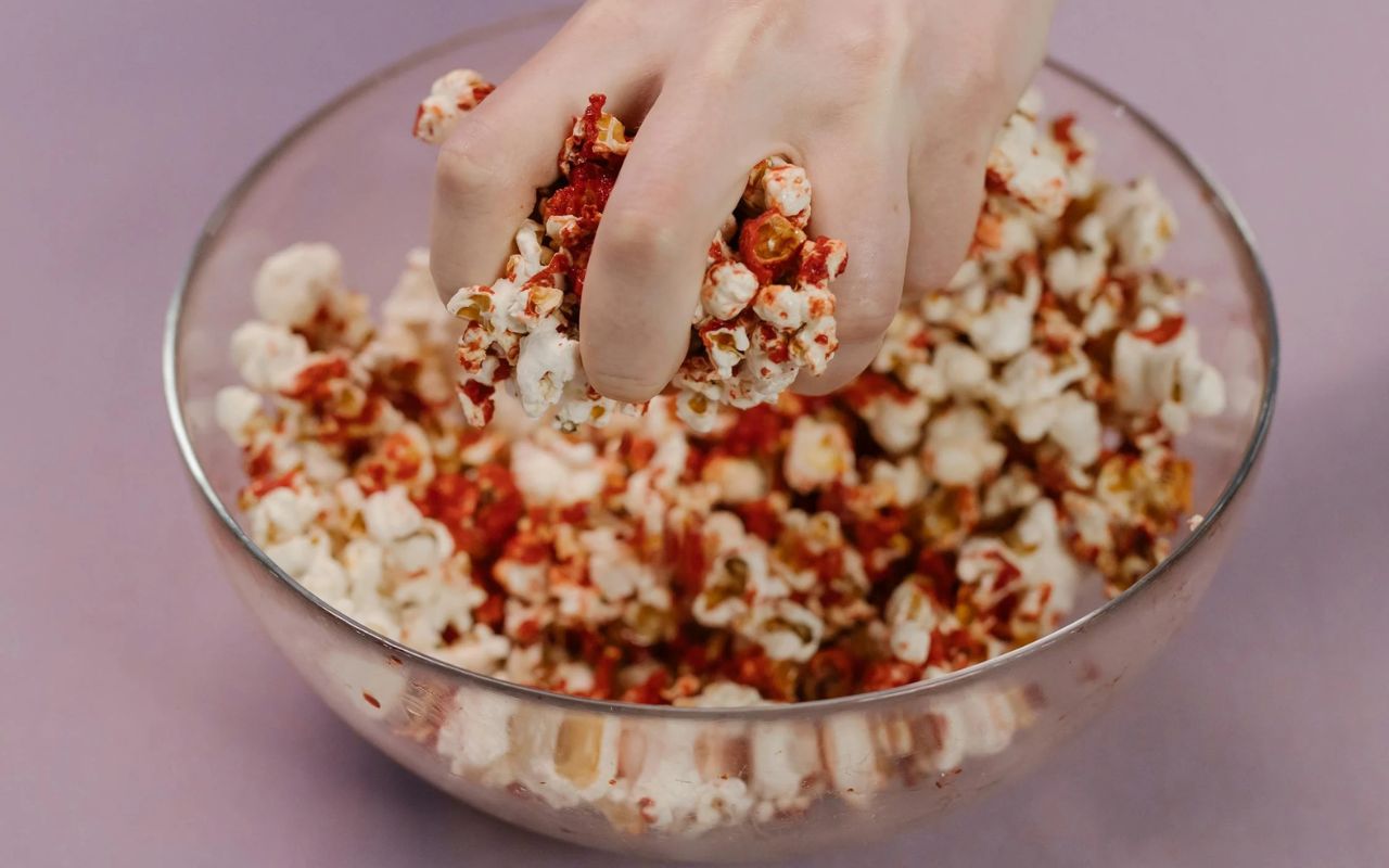 Hand grabbing spicy coated popcorn from a glass bowl