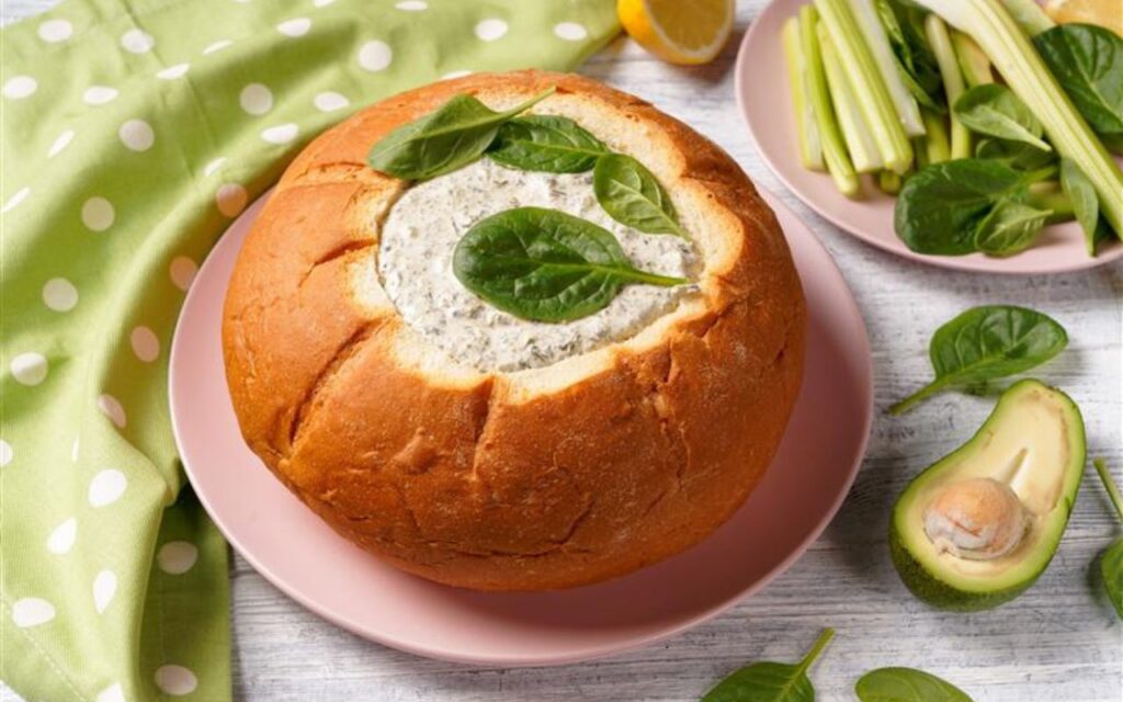 Creamy spinach dip bread bowl, topped with spinach—celery and avocado on the side