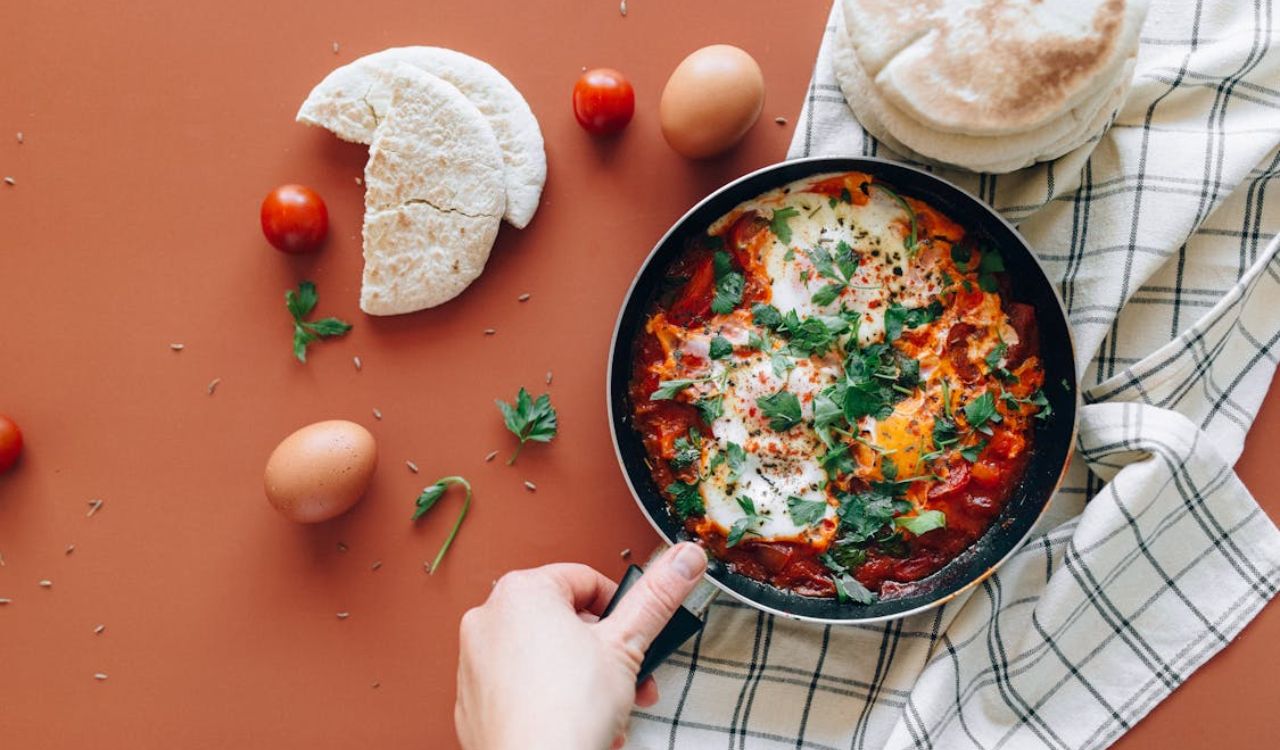 Person Holding a Black Ceramic Pan with Shakshuka