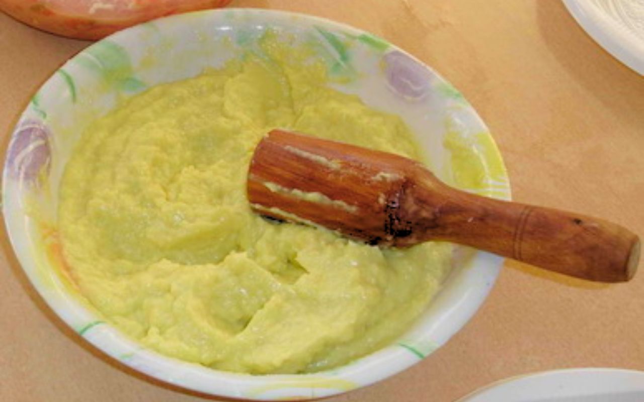 A bowl of mashed toum with a wooden pestle