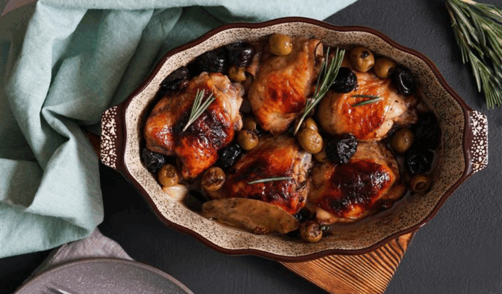 Baked chicken with olives, prunes, and rosemary in a serving dish.