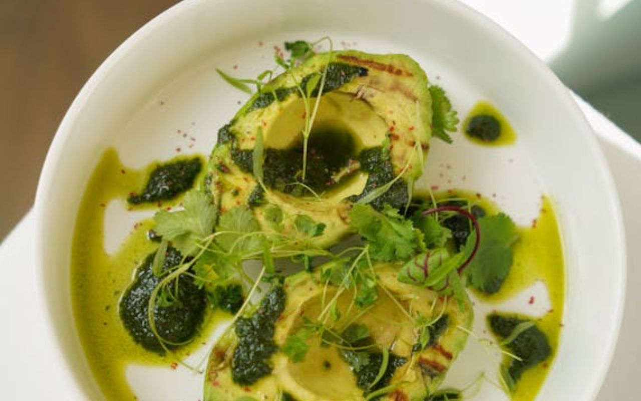 Grilled avocado halves drizzled with pesto and garnished with fresh herbs