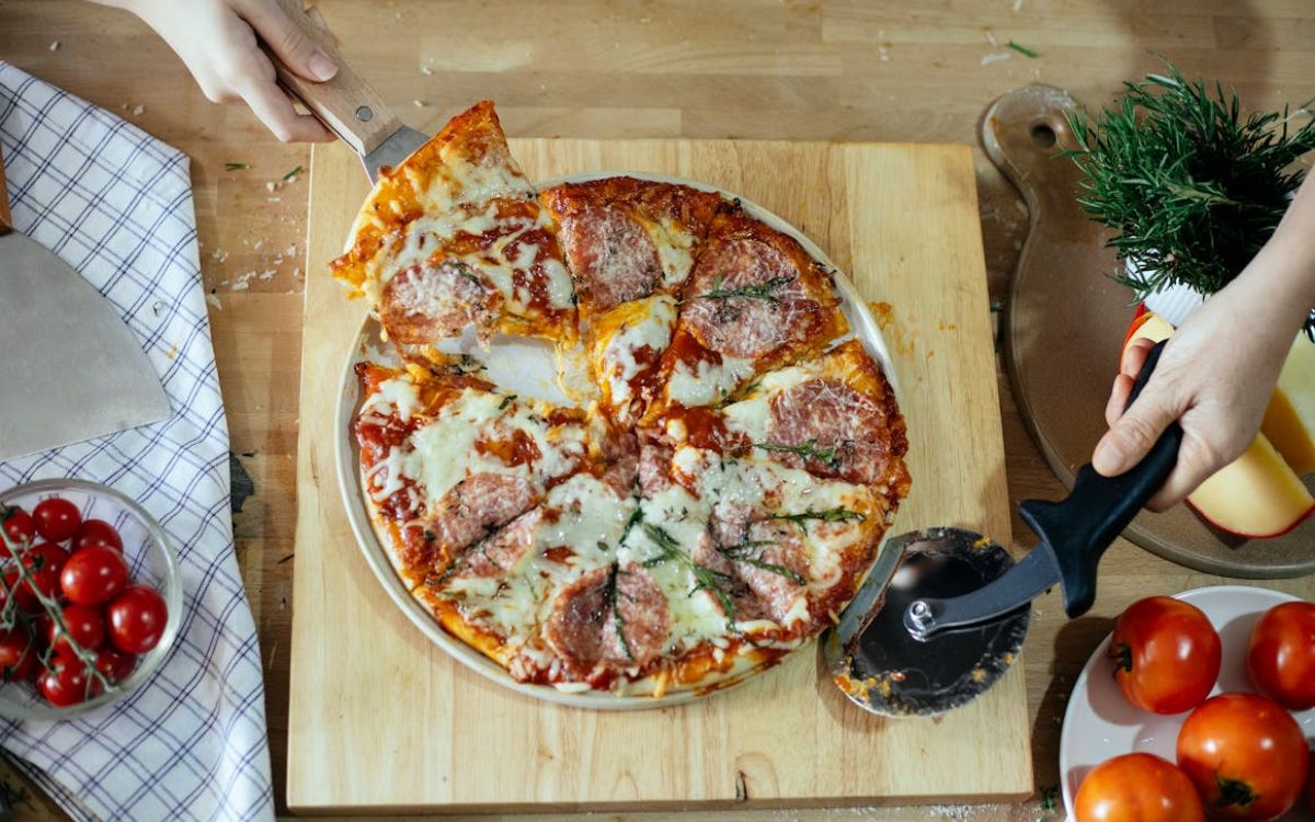 Homemade salami pizza on a board, one slice lifted
