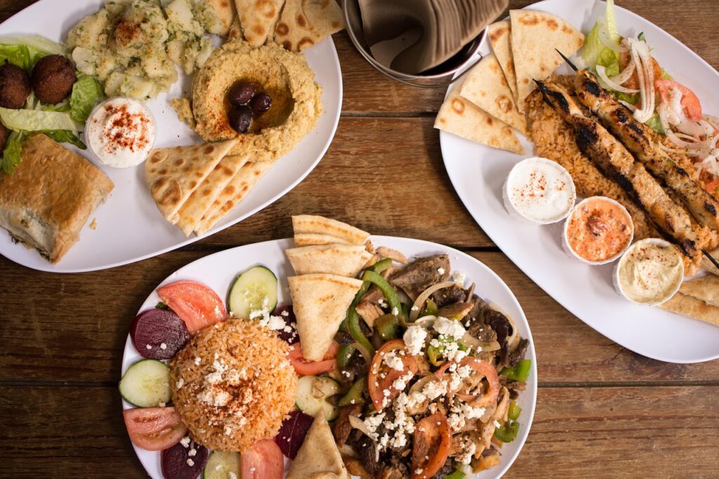 A platter with three small bowls of different hummus flavors, surrounded by pita wedges and veggies.