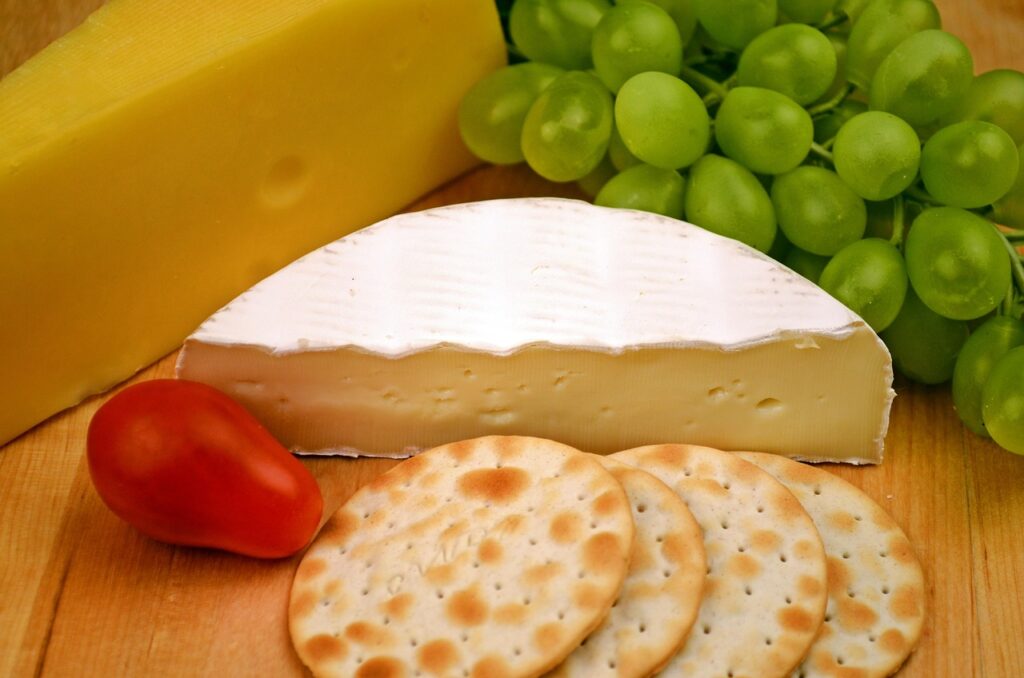 A cheese board with a variety of cheeses, grapes, and crackers.