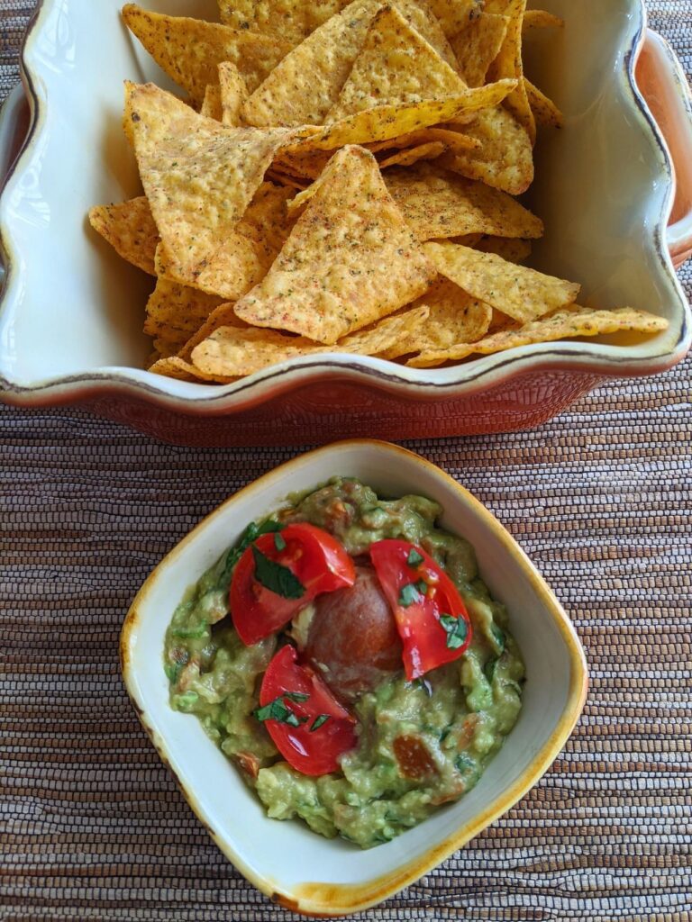 A bowl of guacamole surrounded by tortilla chips and lime wedges.